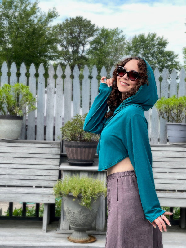 Woman in teal cute cropped sun safe upf 50+ hoodie for travel , with extra large hood and glovelettes for hand protection
