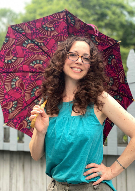 Happy woman standing by a pool in a garden in a cool tank top holding a colorful parasol