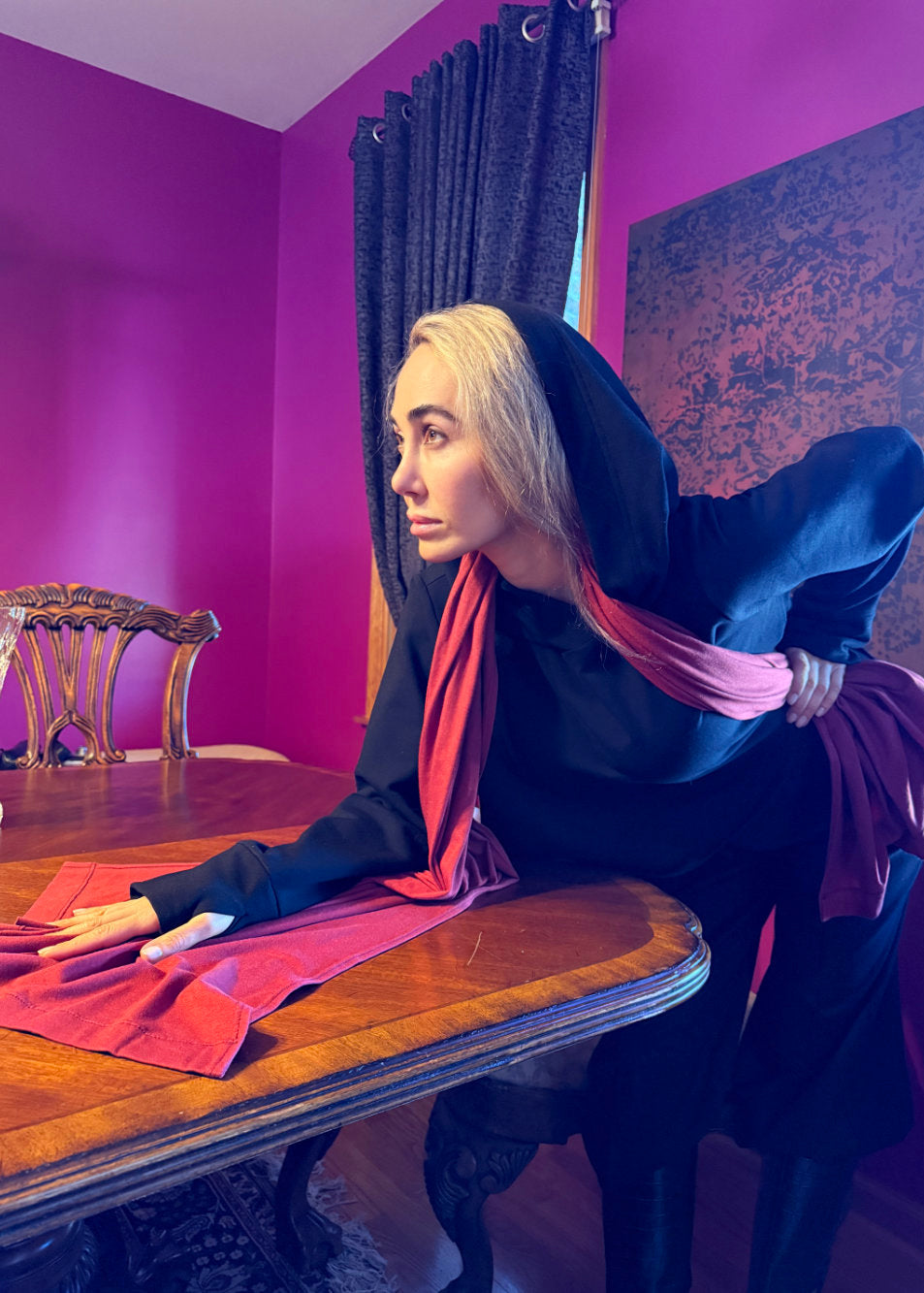 Woman wearing a black hoodie with a red scarf standing at a table in a room with purple walls.