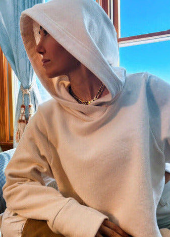 Person wearing a beige hoodie sitting indoors with a window in the background